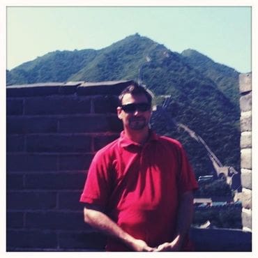 A man in red shirt standing next to a wall.