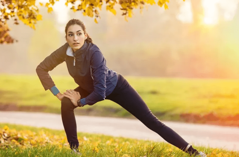 A woman stretching in the grass near a tree.