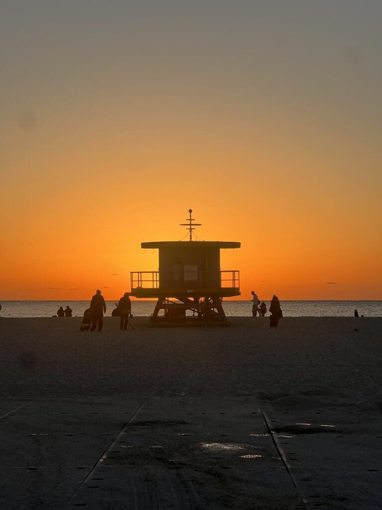 A beach with people sitting on the sand and an orange sky