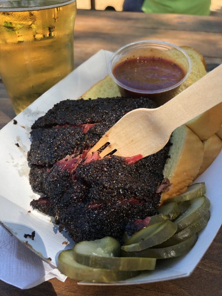 A close up of a plate with meat and pickles