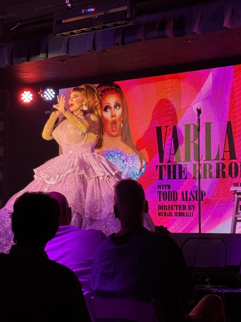 A woman in pink dress on stage with a poster of rupaul.