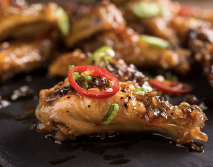 A close up of some chicken wings with chili peppers